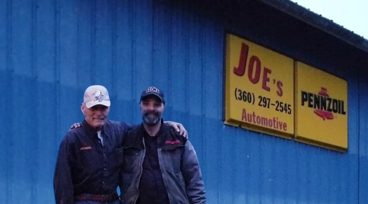 Two men standing outside Joe’s Automotive and Pennzoil sign on a blue building