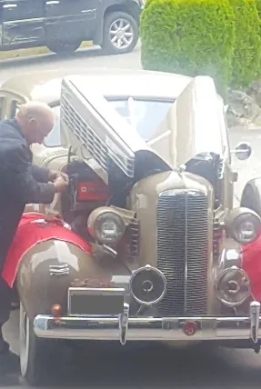 Person working on the front of a vintage red car in a driveway with the hood open