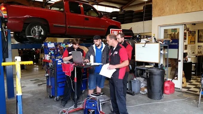 Auto repair shop with a red car on a lift and three mechanics reviewing paperwork