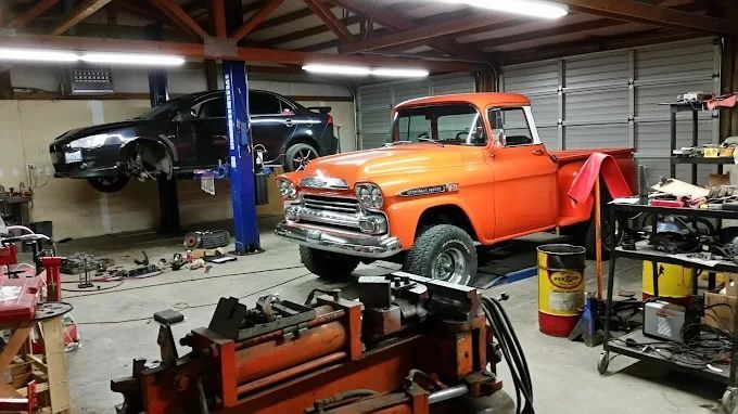 Classic orange pickup in auto shop with blue car on a lift and tools in the foreground