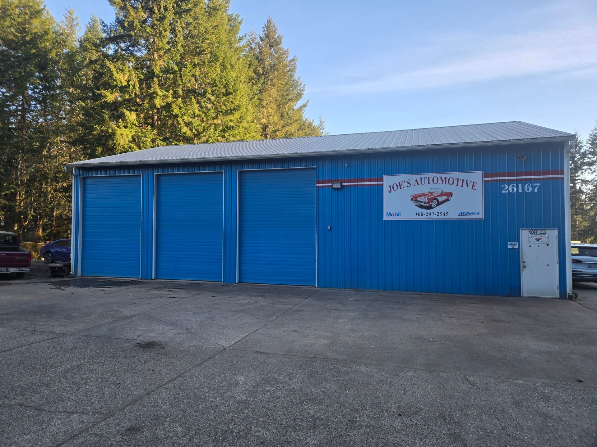Blue storage building with white sign and closed doors in a gravel lot, trees behind it.