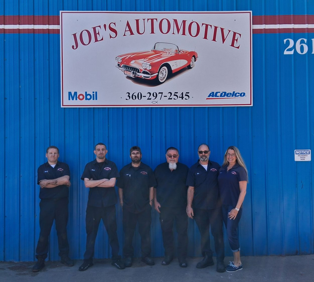 Six people standing outside Joe’s Automotive under a sign on a blue building.