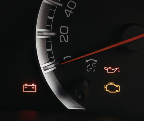 Car dashboard gauge with red needle and warning lights for battery, oil, and engine illuminated