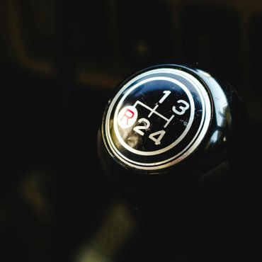 Close-up of a manual car gear shift knob with a 5-speed shift pattern.