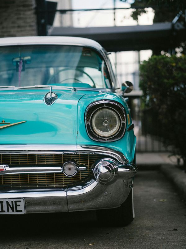 Front view of a turquoise vintage car parked outdoors, showing chrome details and a round headlight