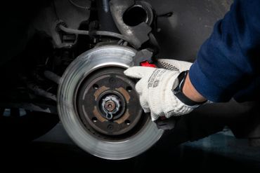 Gloved hand inspecting a car’s front brake rotor and caliper in a dark garage.
