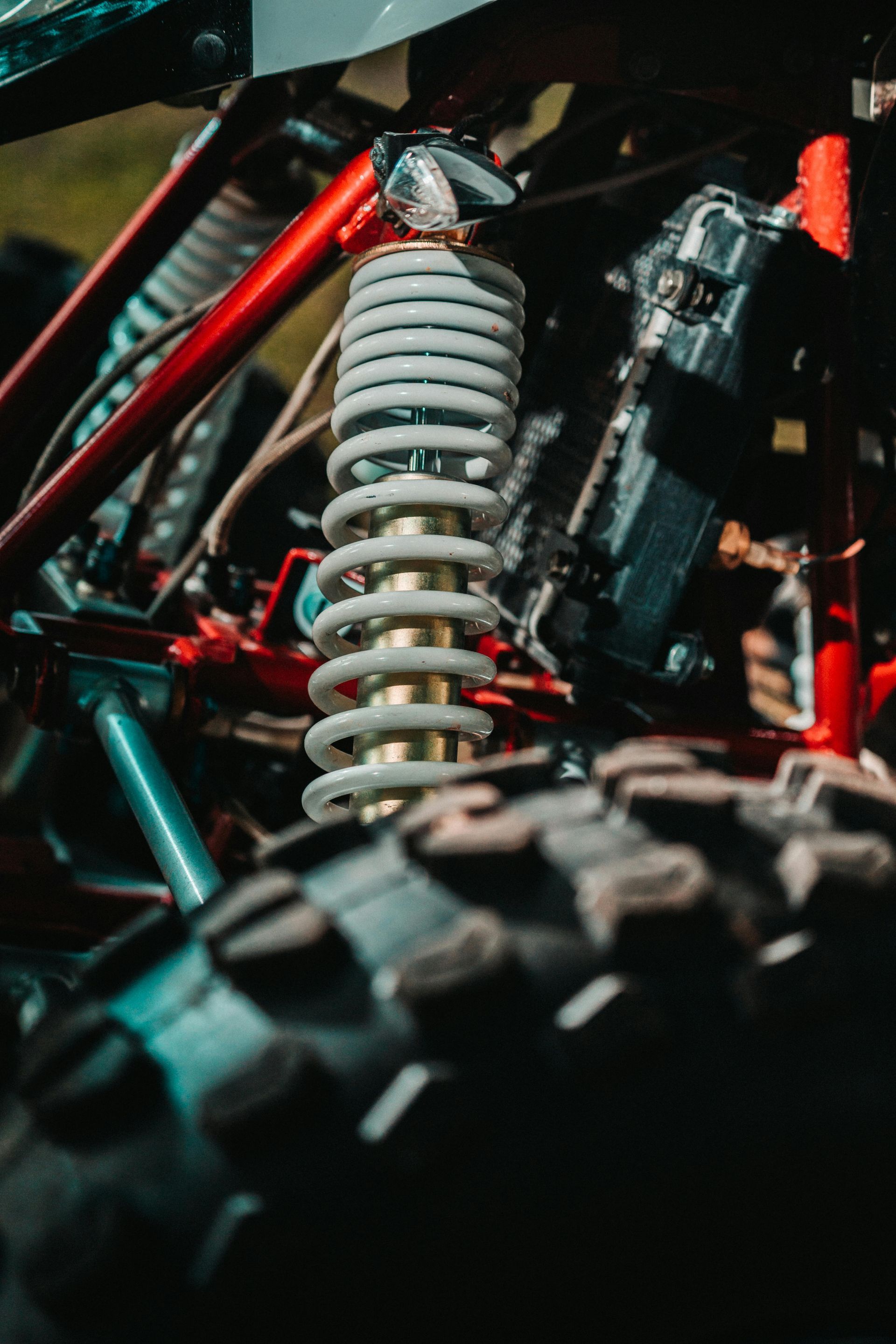 Close-up of a vehicle suspension coil spring and shock absorber with red and black frame parts
