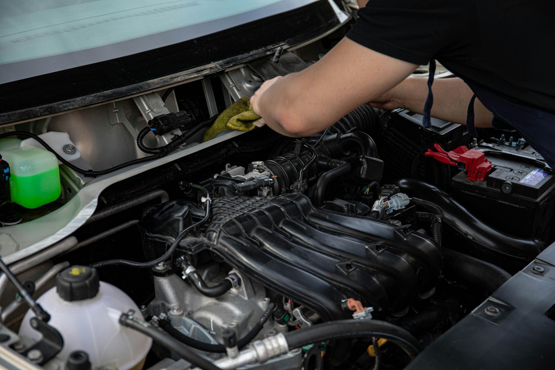 Person working on a car engine in an open hood compartment, with tools and parts visible