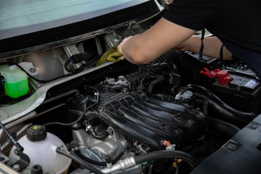 Person working in a car engine bay, cleaning or repairing components under the hood.
