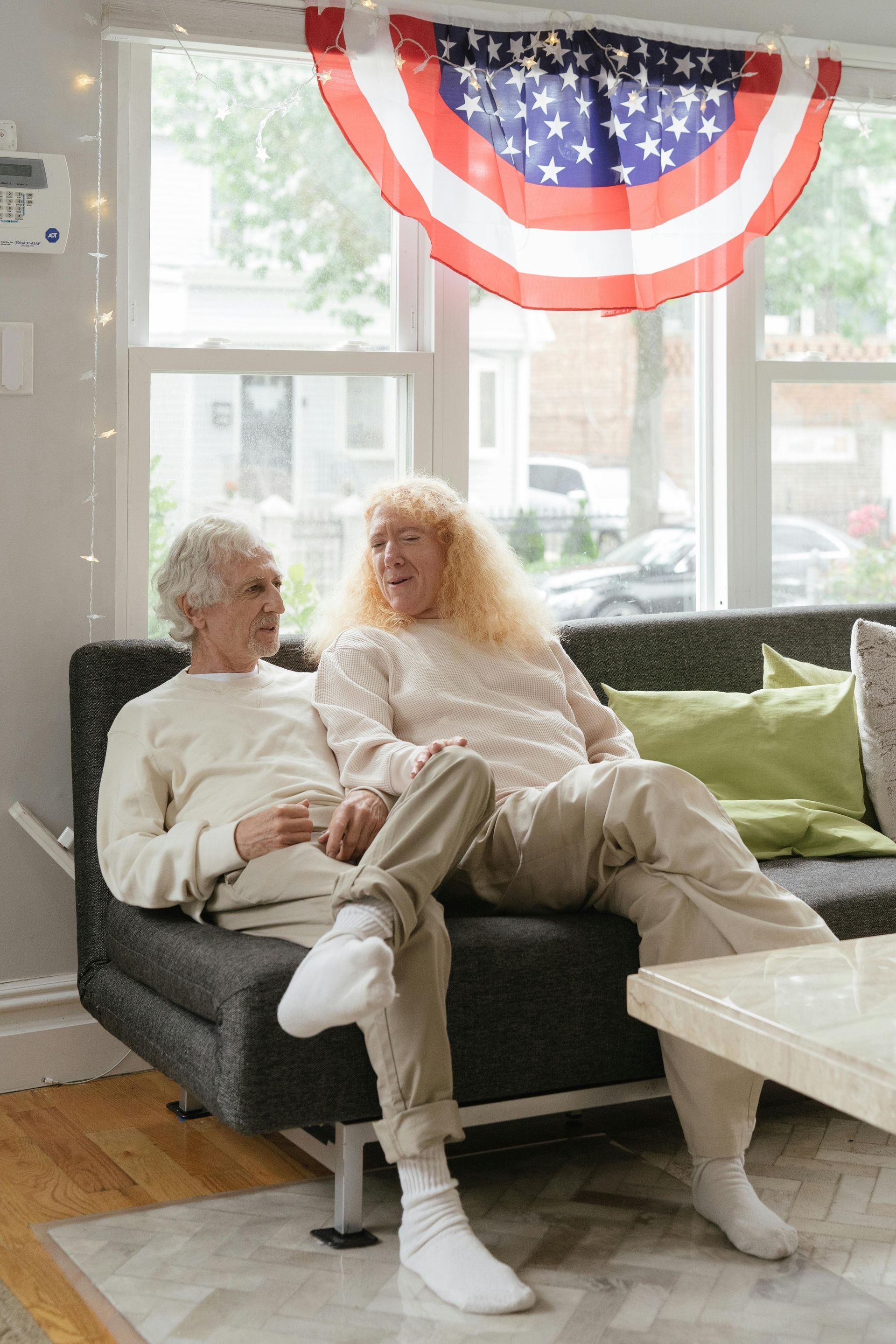 A man and a woman are sitting on a couch in front of an american flag.