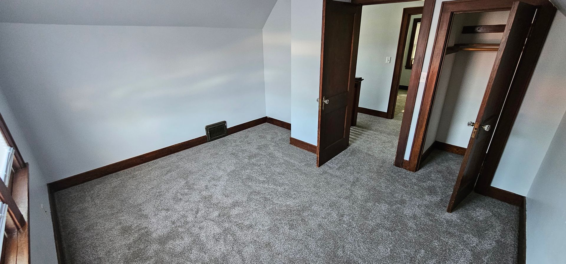 Empty carpeted room with white walls, dark trim, and an open doorway to a hallway
