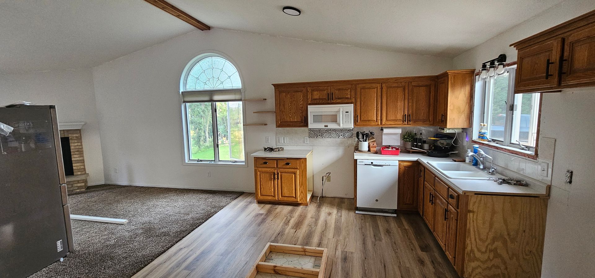 Empty kitchen-living area with wood cabinets, white appliances, and a large arched window