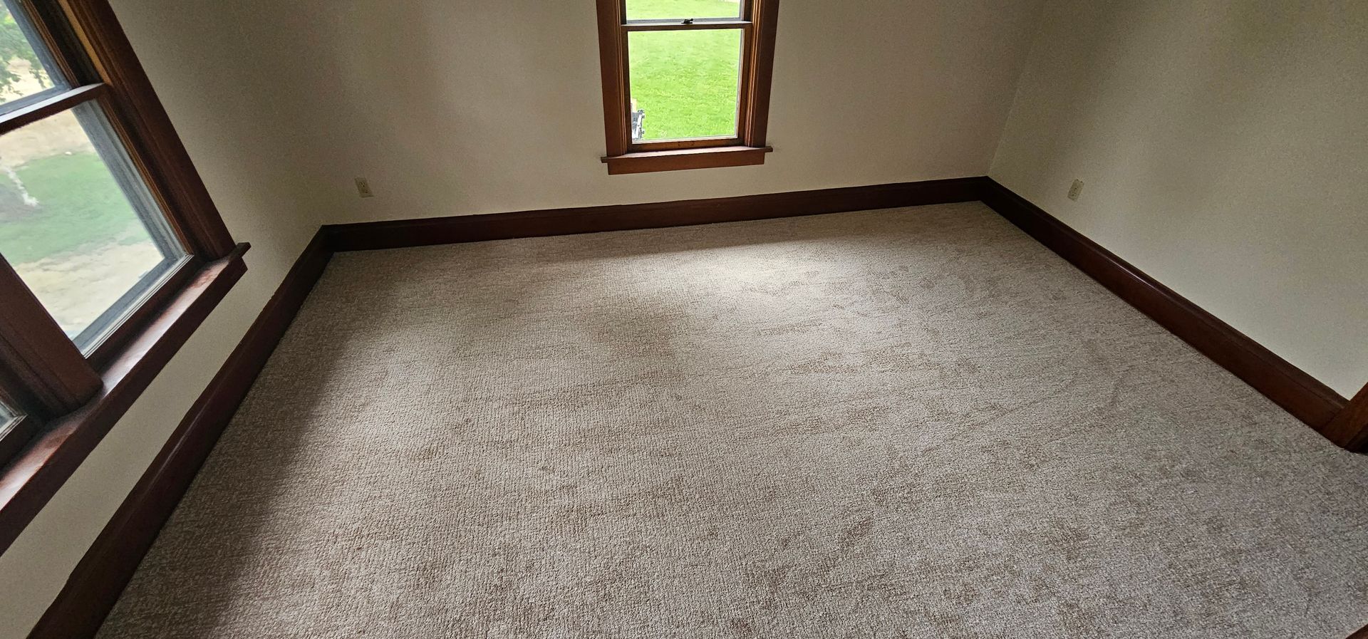Empty carpeted room with beige walls, brown trim, and three small windows letting in daylight