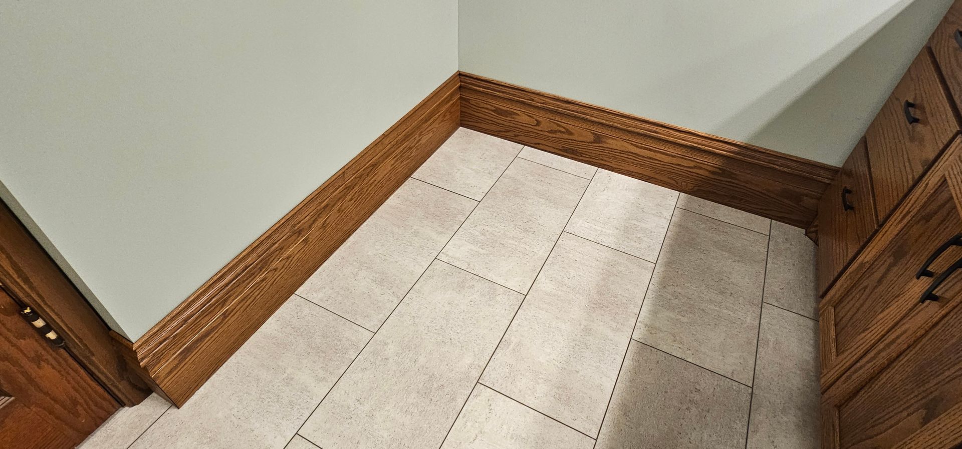 Corner of a tiled floor with wood baseboards and a cabinet in a kitchen or hallway
