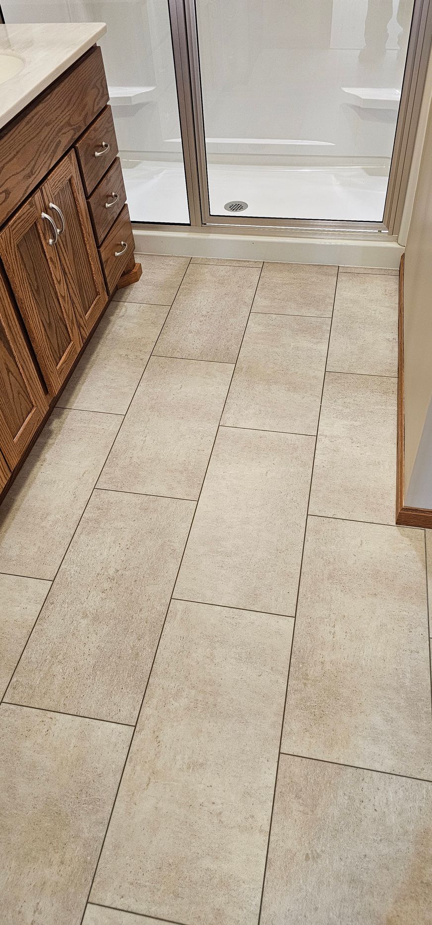 Narrow beige-tiled hallway with a wooden cabinet on the left and a doorway at the end.