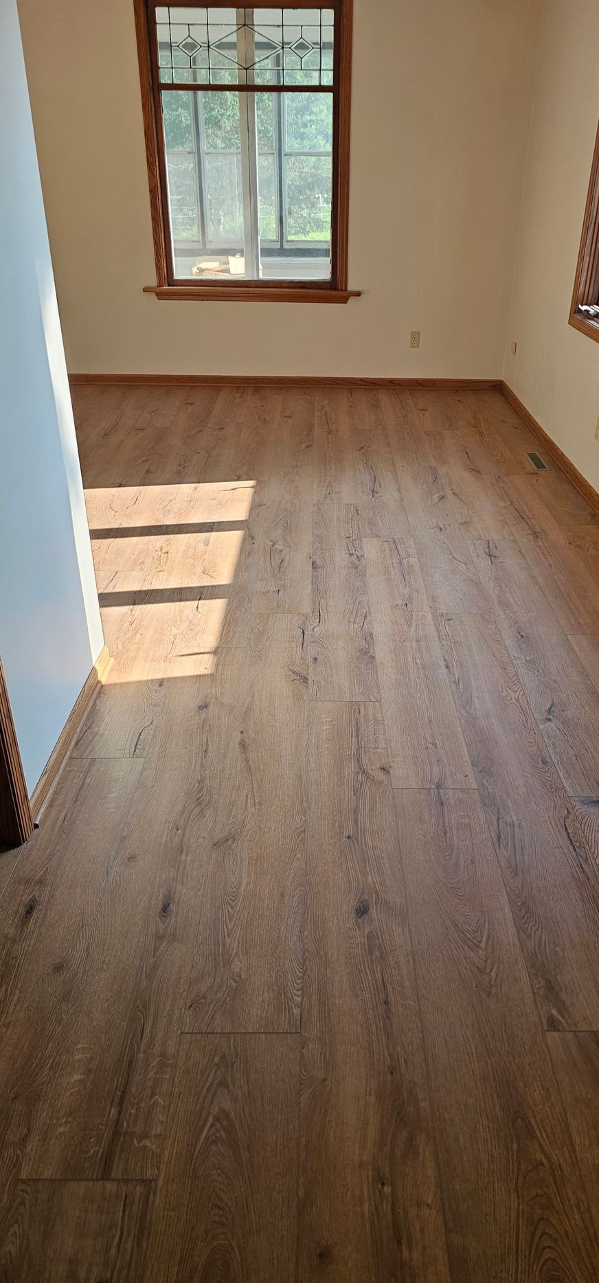 Empty sunlit room with wood-look flooring and a window casting light on the floor