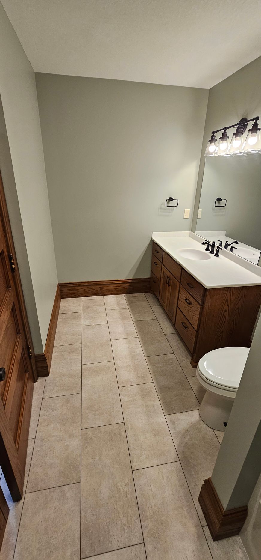 Small beige bathroom with tiled floor, wood vanity, mirror, and toilet.