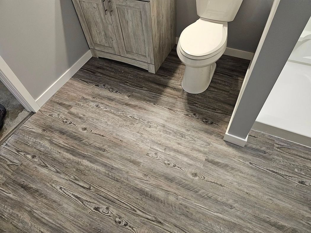 Small bathroom with gray wood-look flooring, a toilet, and a rustic cabinet beside the wall.