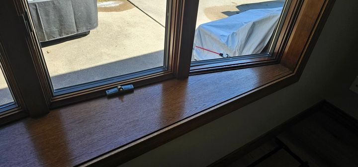 Sunlit window ledge with a woven mat and a blue-covered object outside on a patio
