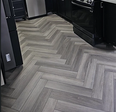 Gray herringbone tile floor in a modern kitchen with black cabinets and appliances