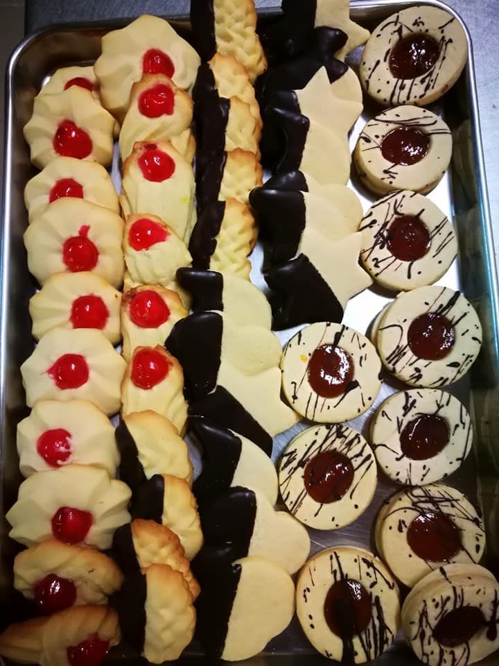 Assortimento di biscotti e pasticcini decorati, disposti in file ordinate su un vassoio.
