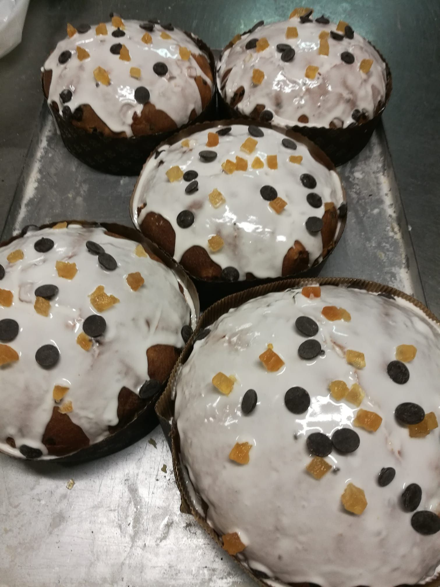 Cinque torte rotonde ricoperte di glassa bianca, decorate con gocce di cioccolato e zuccherini arancioni, disposte su un vassoio di metallo.