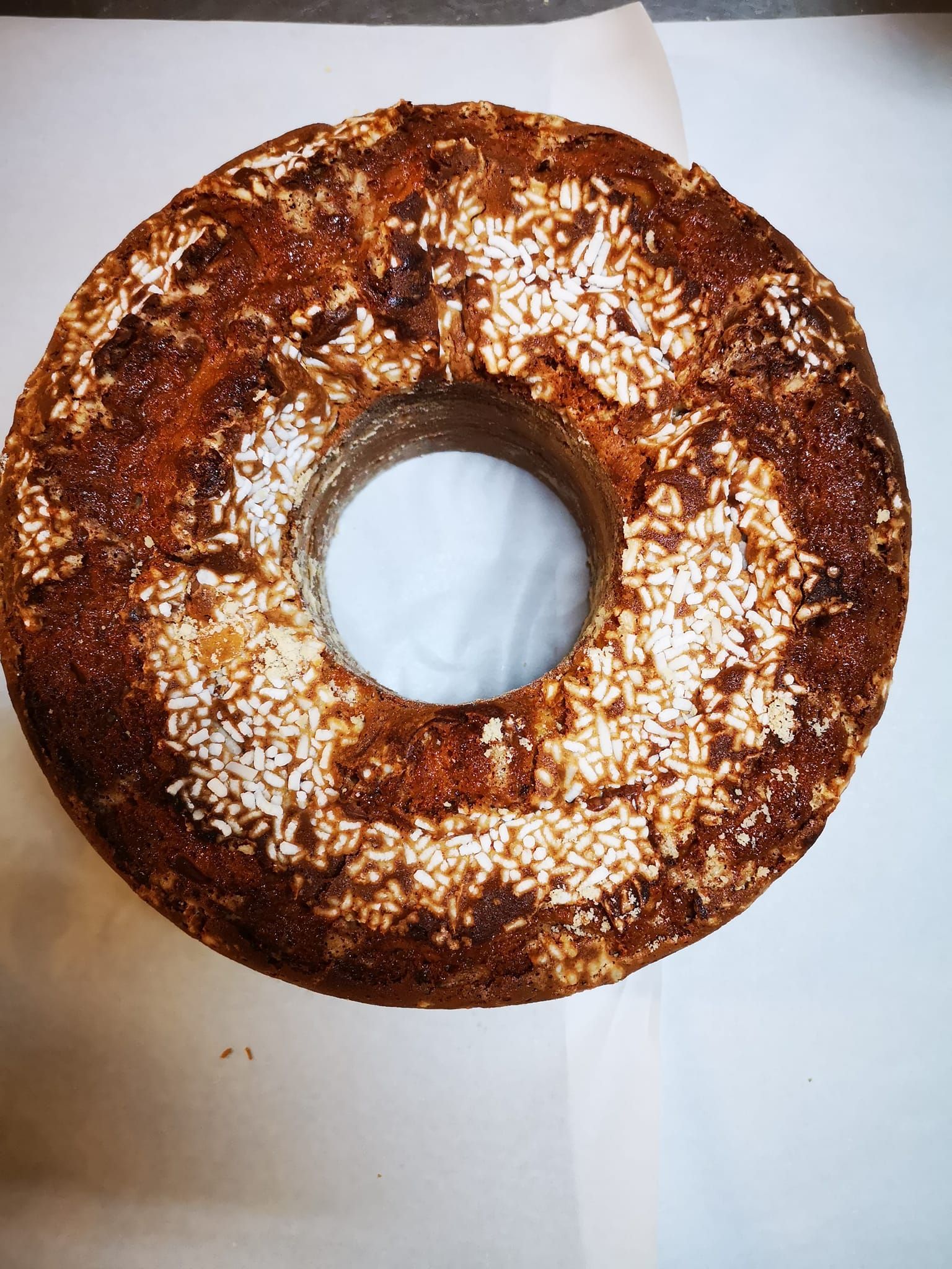 Torta bundt rotonda ricoperta di glassa al cioccolato, con un foro centrale, spolverata di zucchero a velo e disposta su carta bianca.