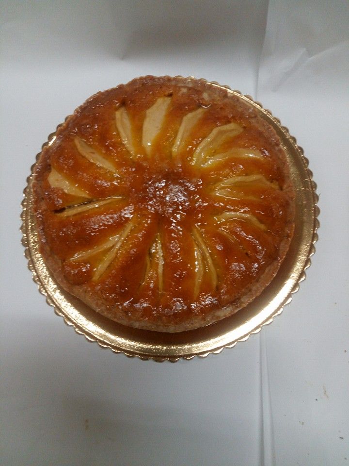 Crostata rotonda di frutta glassata, cotta in uno stampo di alluminio dorato su una superficie bianca.