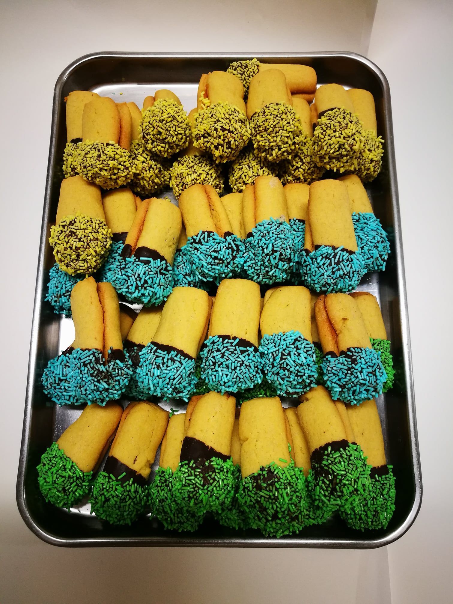 Vassoio di rotolini di pasta sfoglia gialla ricoperti di zuccherini blu, verdi e neri.