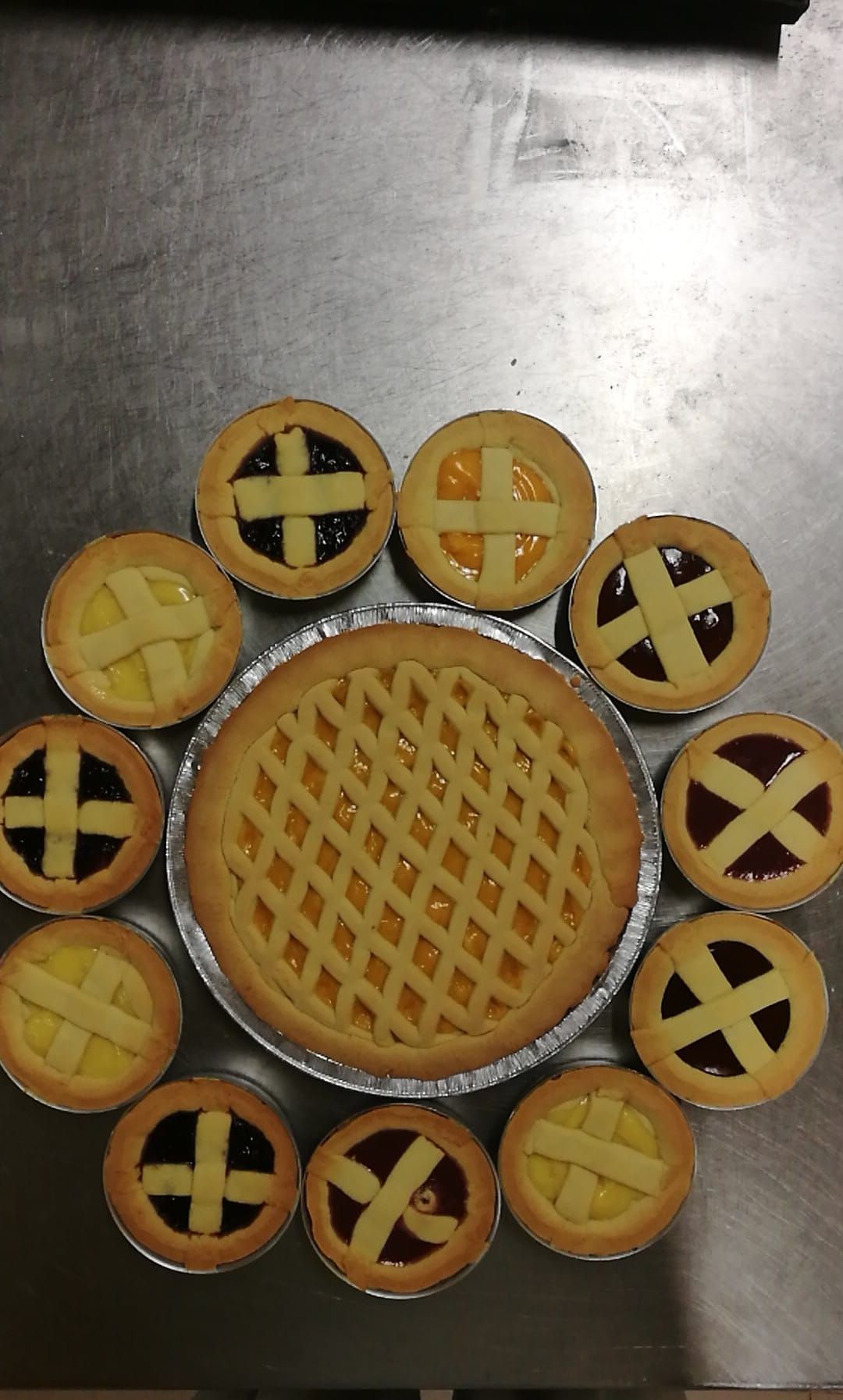 Pasticcini rotondi con copertura a griglia, disposti attorno a una torta più grande su un vassoio di metallo.