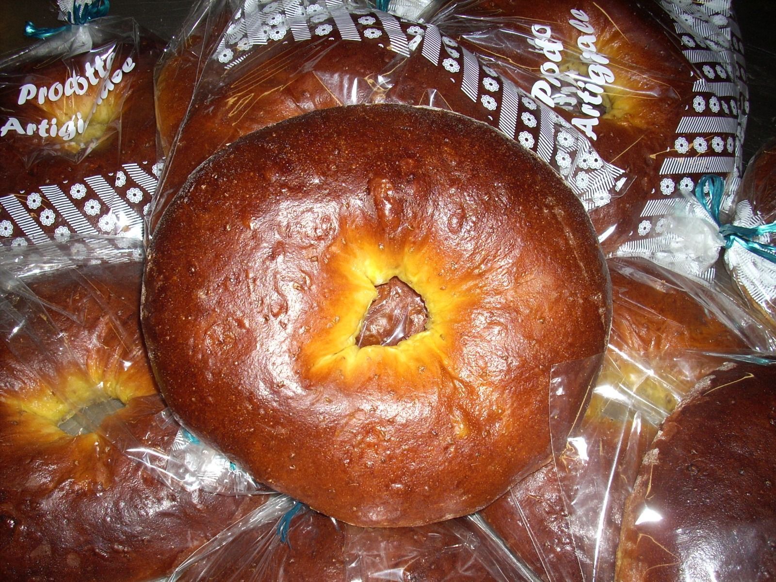 Vassoio di ciambelle lucide marroni a forma di anello, avvolte in un involucro di plastica trasparente.