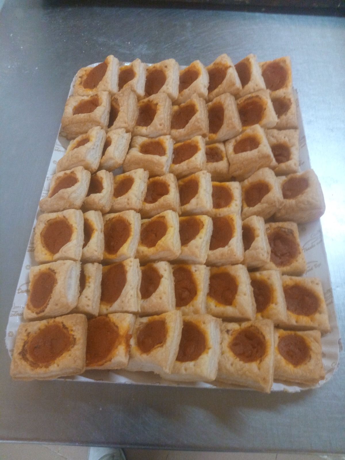 Vassoio di pasticcini quadratini spolverati di polvere arancione, disposti a griglia su una superficie bianca.