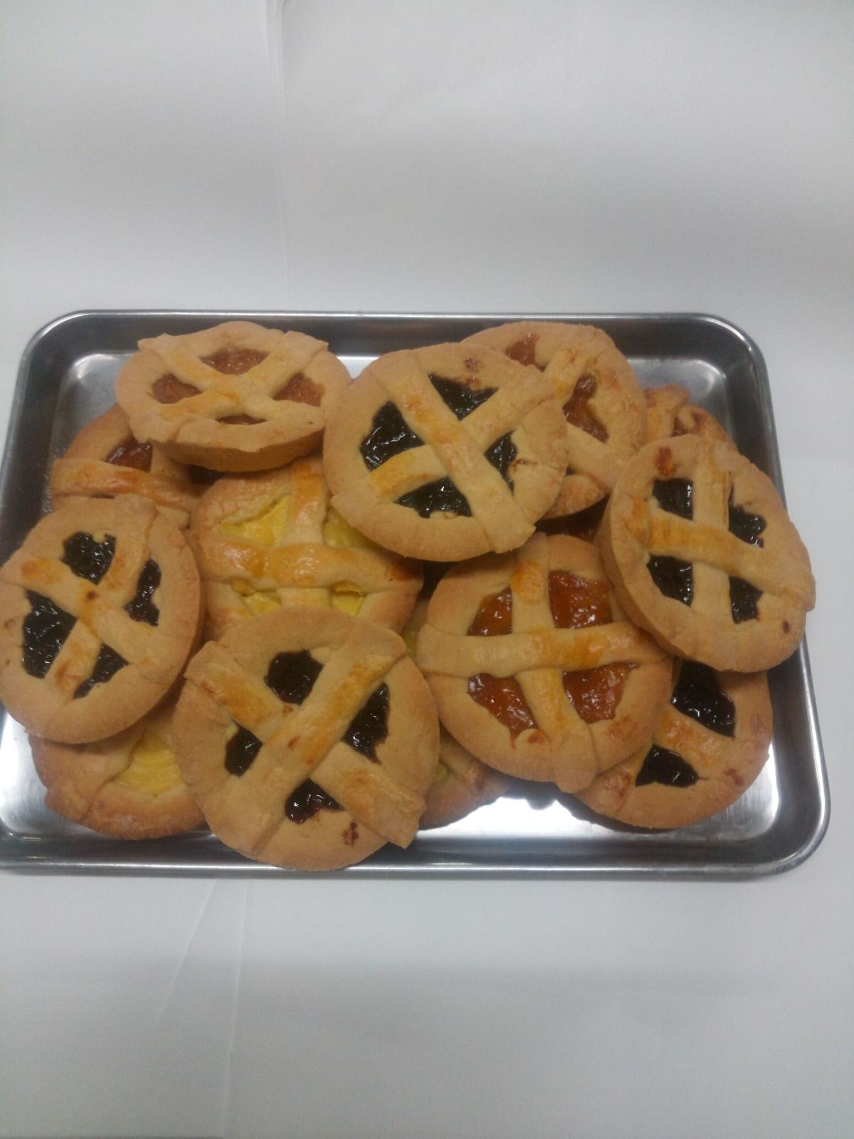 Vassoio di pasticcini rotondi con copertura a griglia, alcuni con ripieno scuro, disposti su un vassoio di metallo.