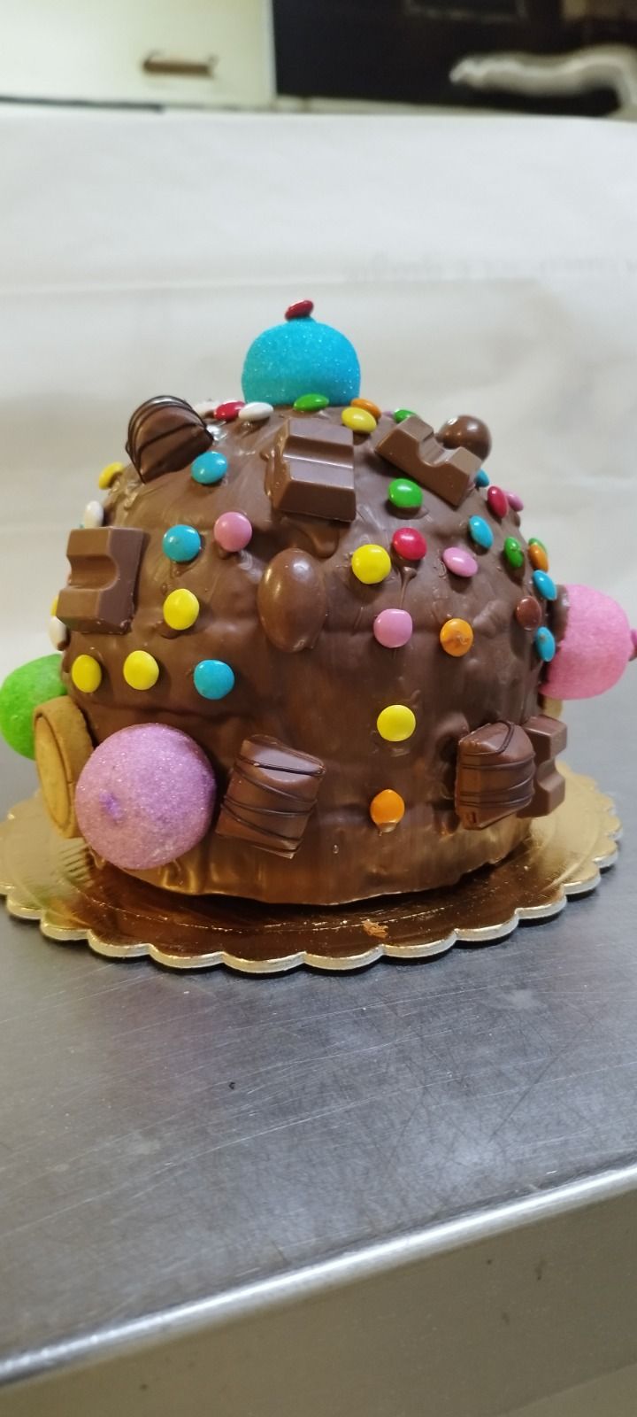 Cupcake al cioccolato decorato con zuccherini colorati, una decorazione blu in cima e una caramella viola su una base dorata.