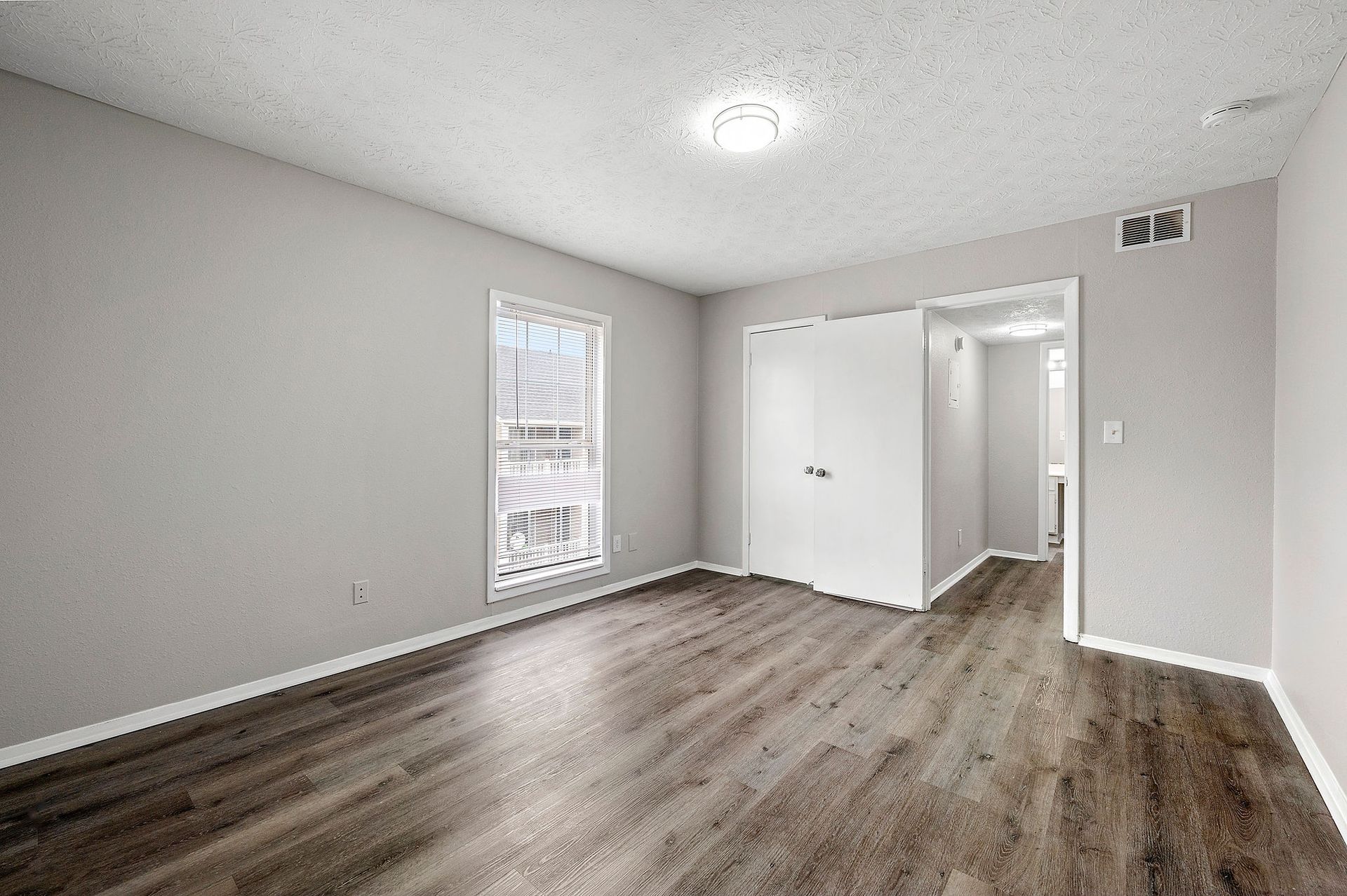 Empty gray room with wood flooring, white trim, ceiling light, and a doorway to a hall