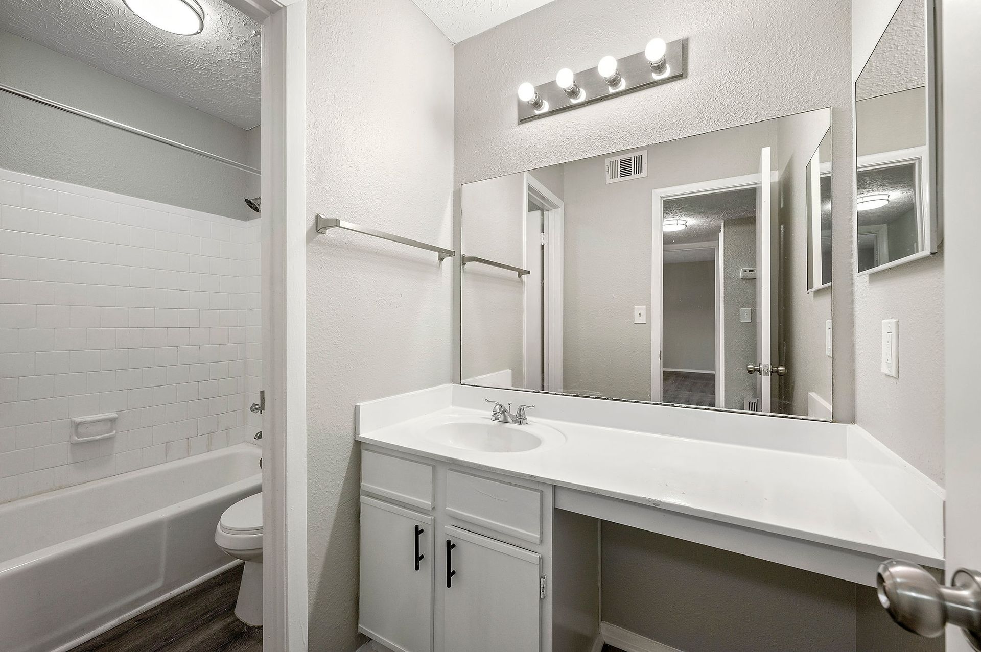 Bright bathroom with vanity, mirror lights, sink, and adjacent bathtub/shower area