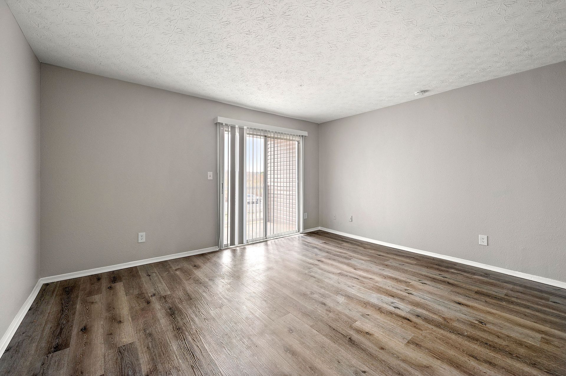 Empty living room with gray walls, wood floor, and sliding glass doors letting in natural light