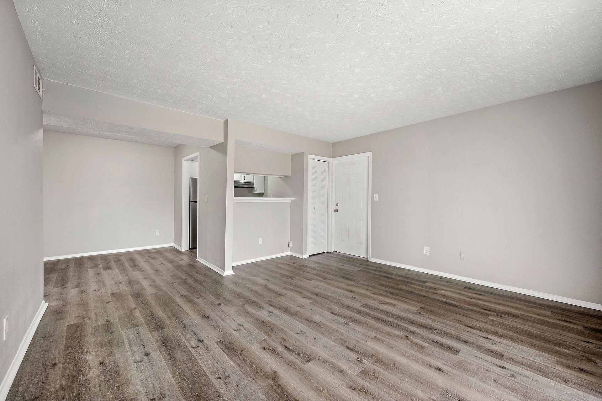 Empty gray living room with wood-look flooring and white doors, viewed from a corner.