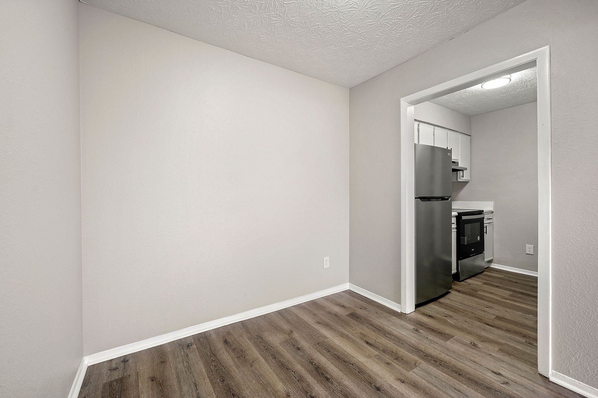 Empty gray room with wood-look flooring and a doorway to a kitchen area