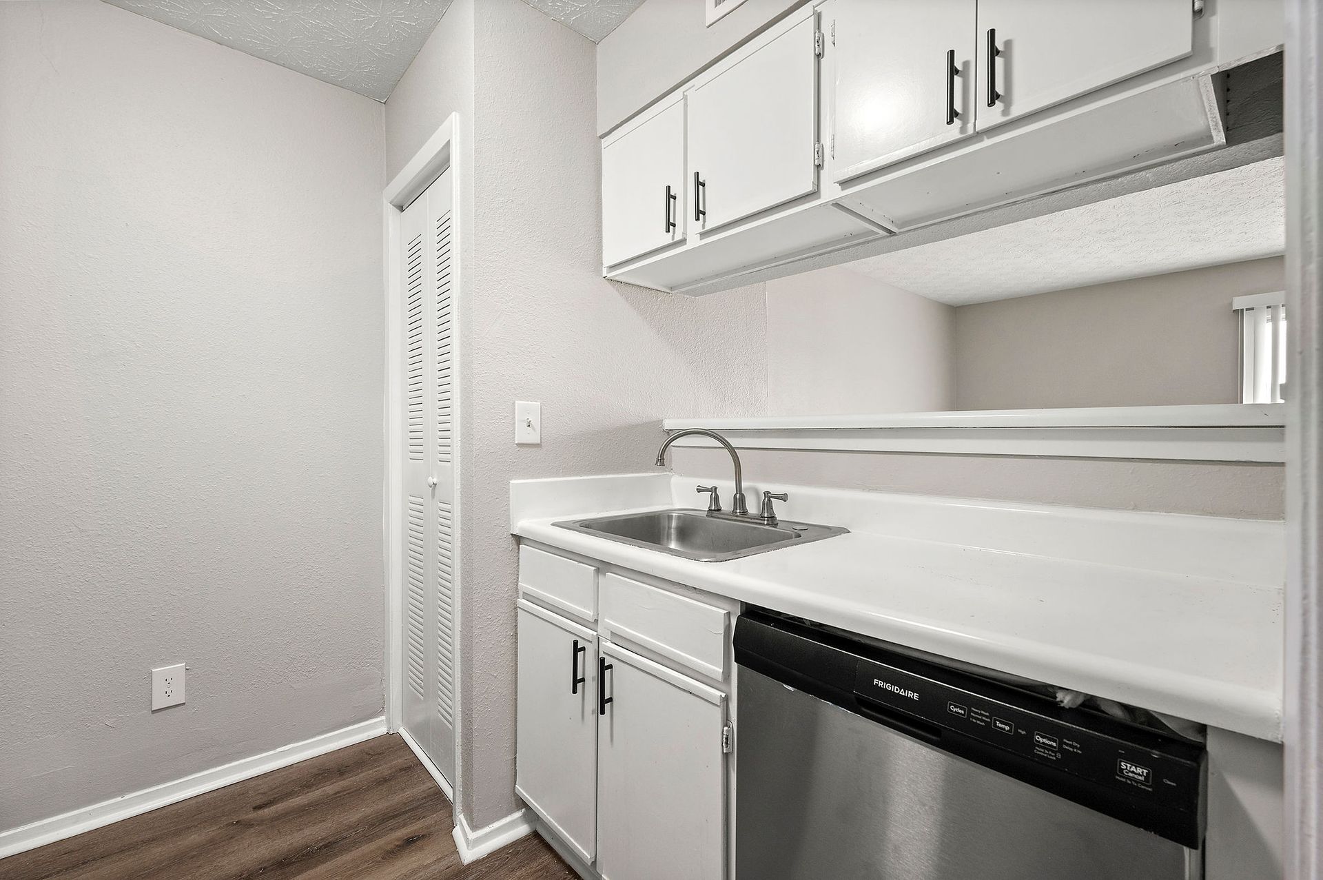 Small white kitchen with sink, countertop, cabinets, dishwasher, and wood floor.