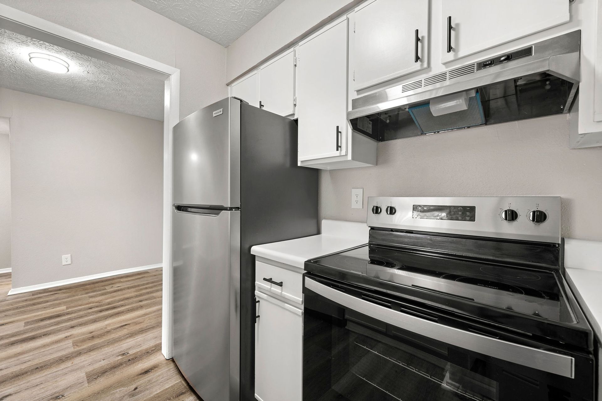Compact kitchen with white cabinets, stainless steel fridge, and black stove/oven beside a hallway.