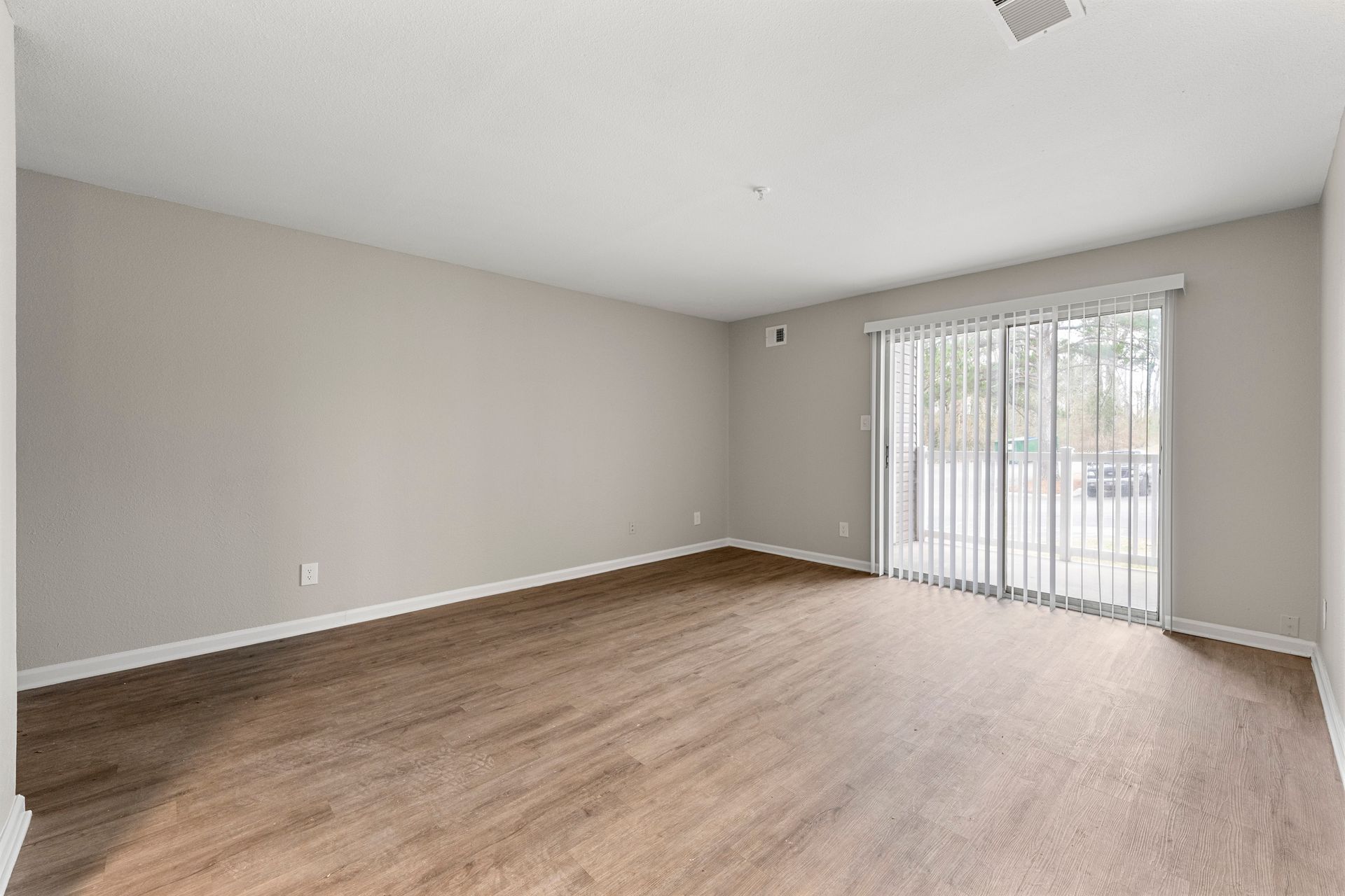 Empty living room with gray walls, wood-look floor, and sliding glass doors to a balcony.