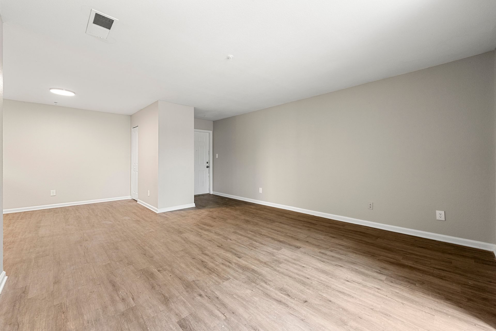 Empty beige room with light wood flooring and white walls, shown in a wide-angle view
