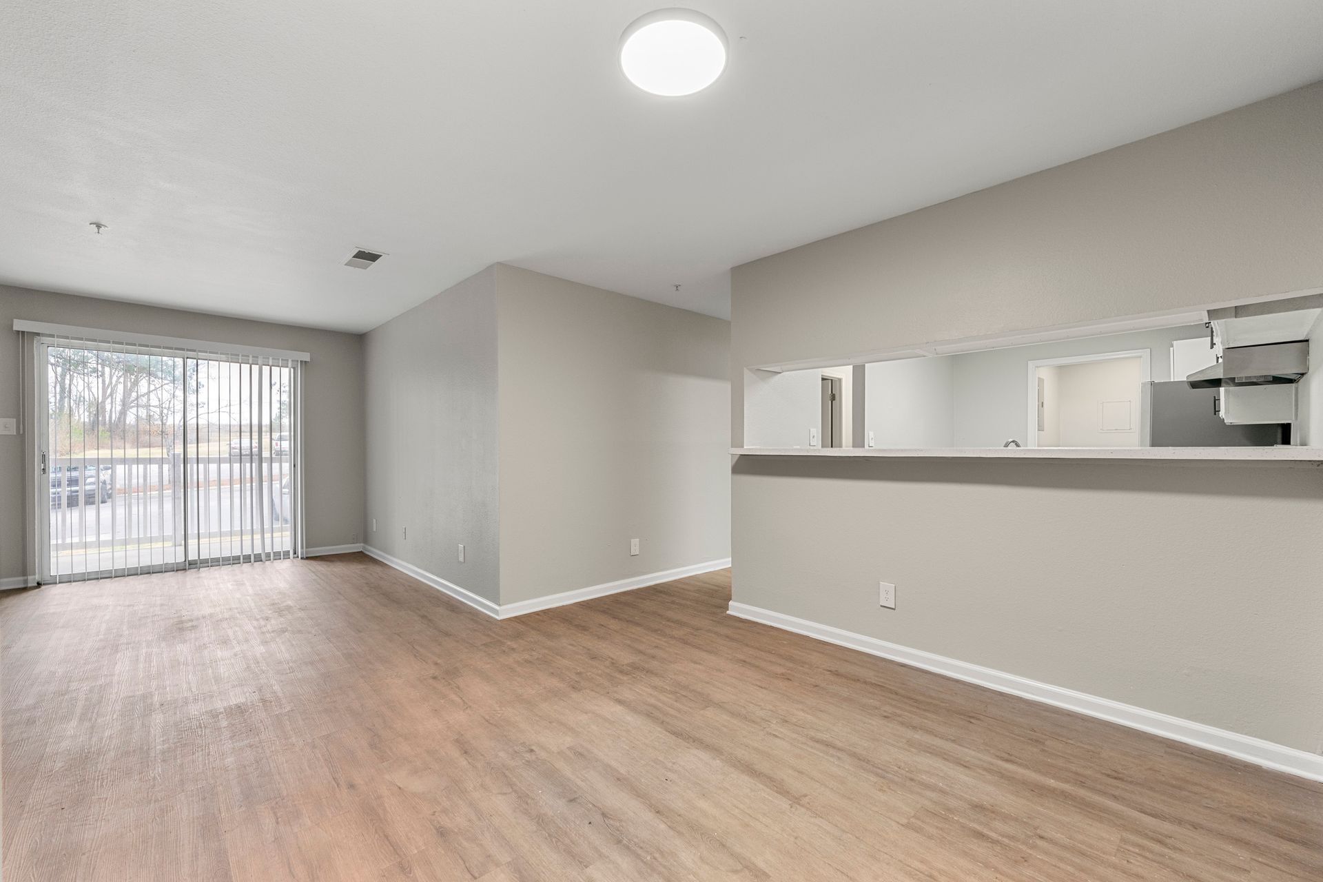 Empty open-plan living room with wood floors, gray walls, and sliding glass door to a balcony.