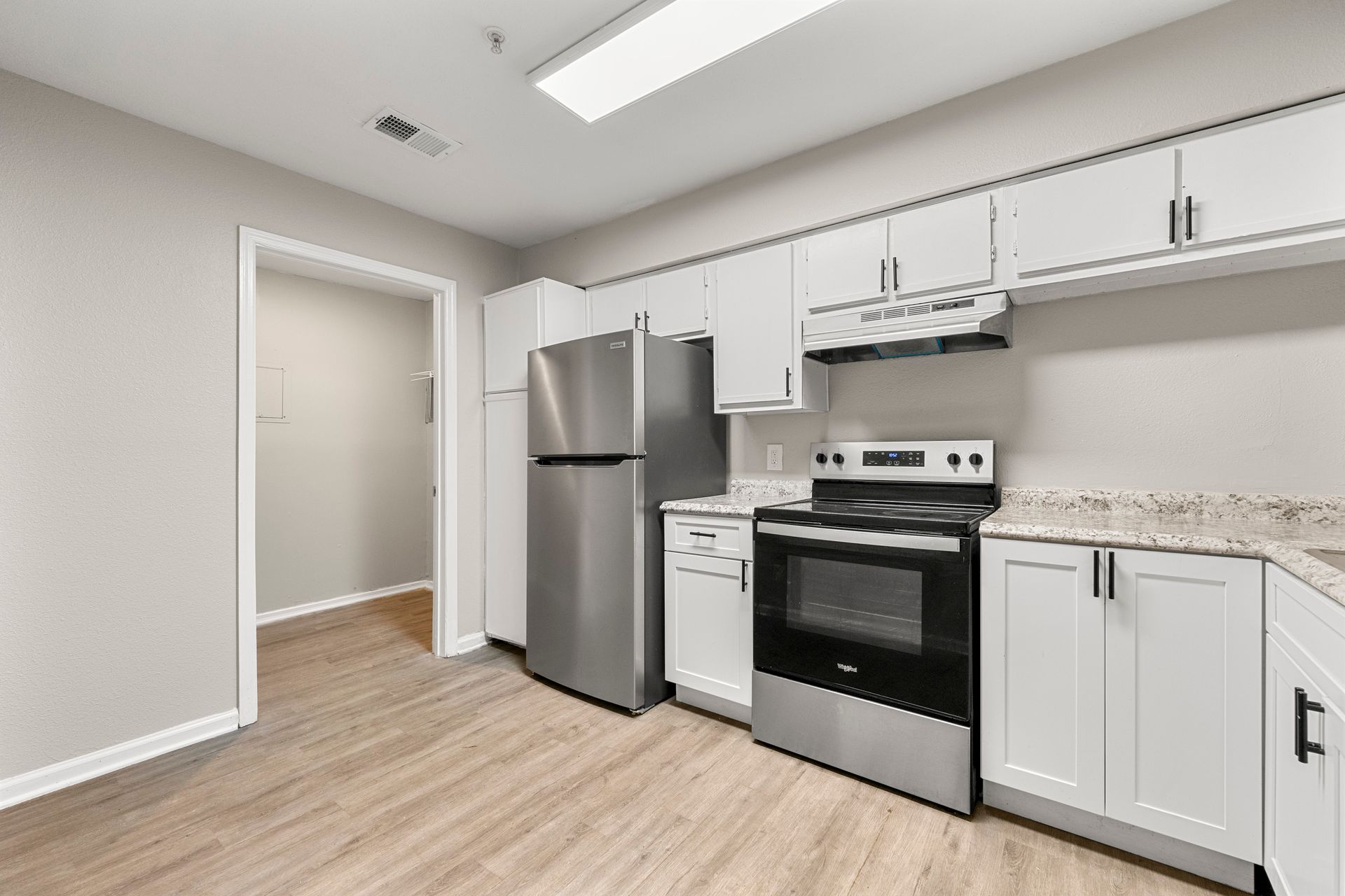 Bright kitchen with stainless steel appliances, white cabinets, and light wood flooring