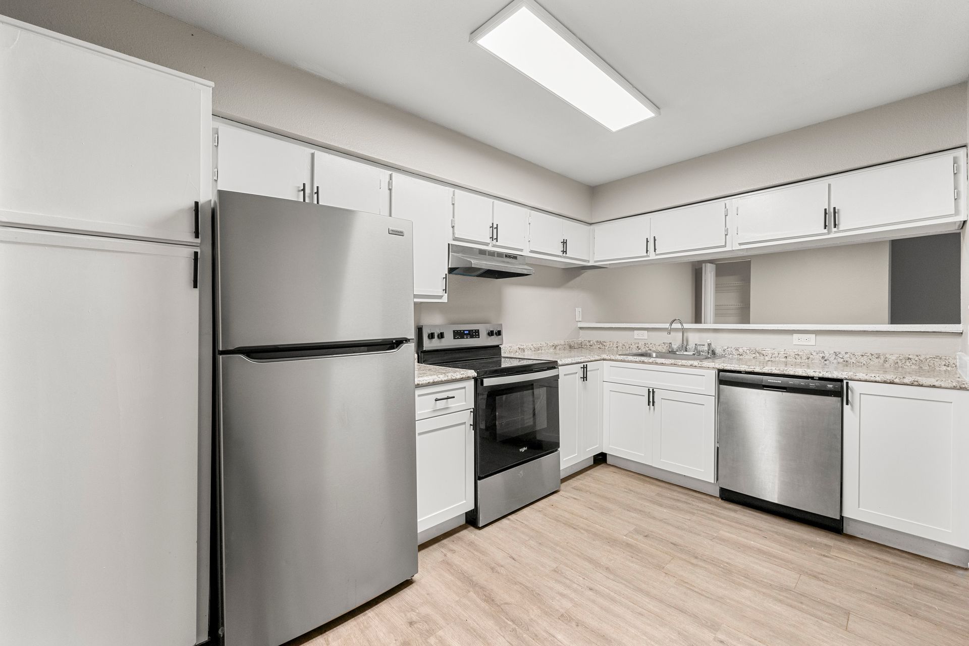 Bright modern kitchen with white cabinets, stainless appliances, and light wood floors.