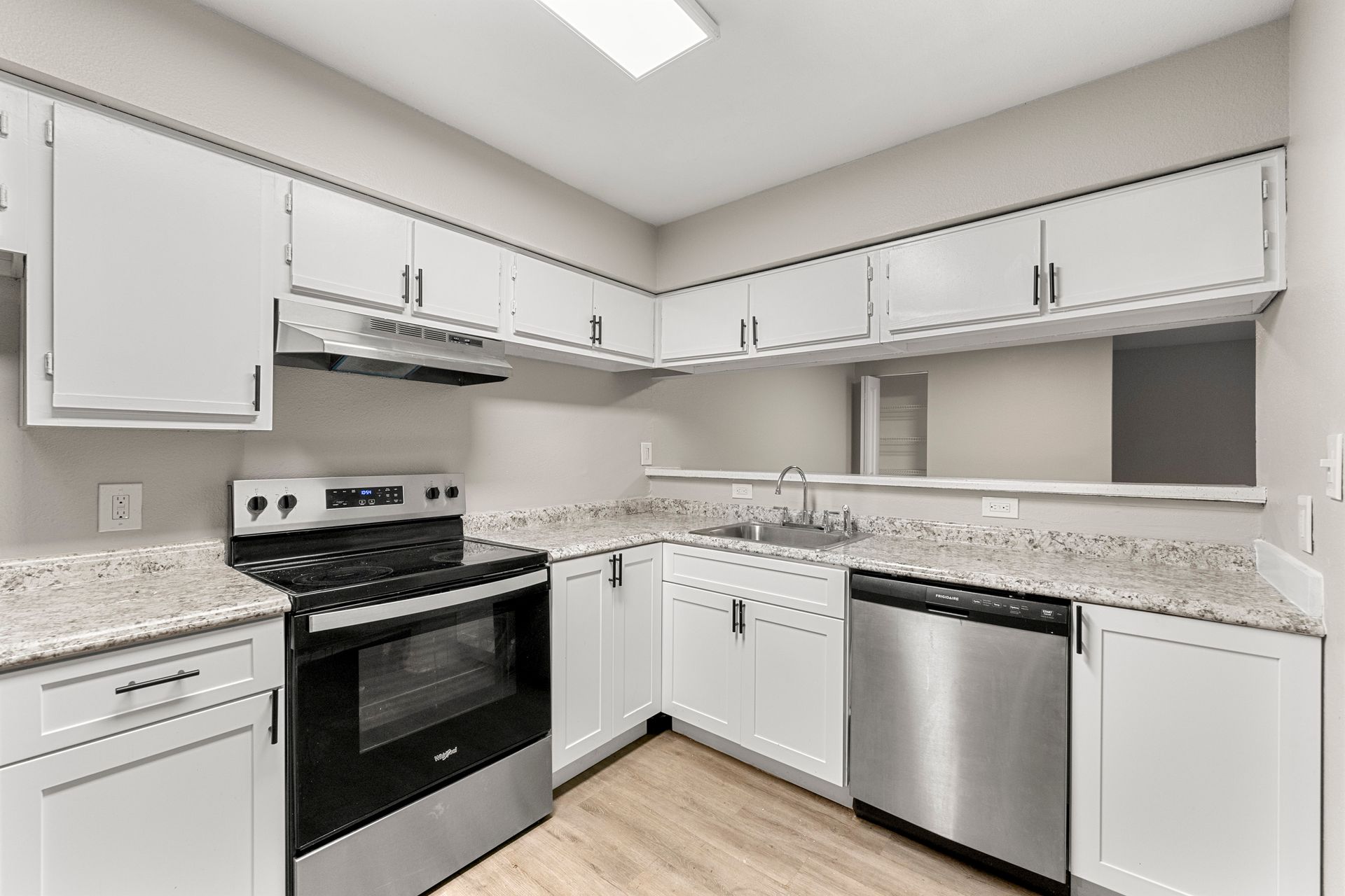 Bright white kitchen with black stove, stainless dishwasher, and light wood floor
