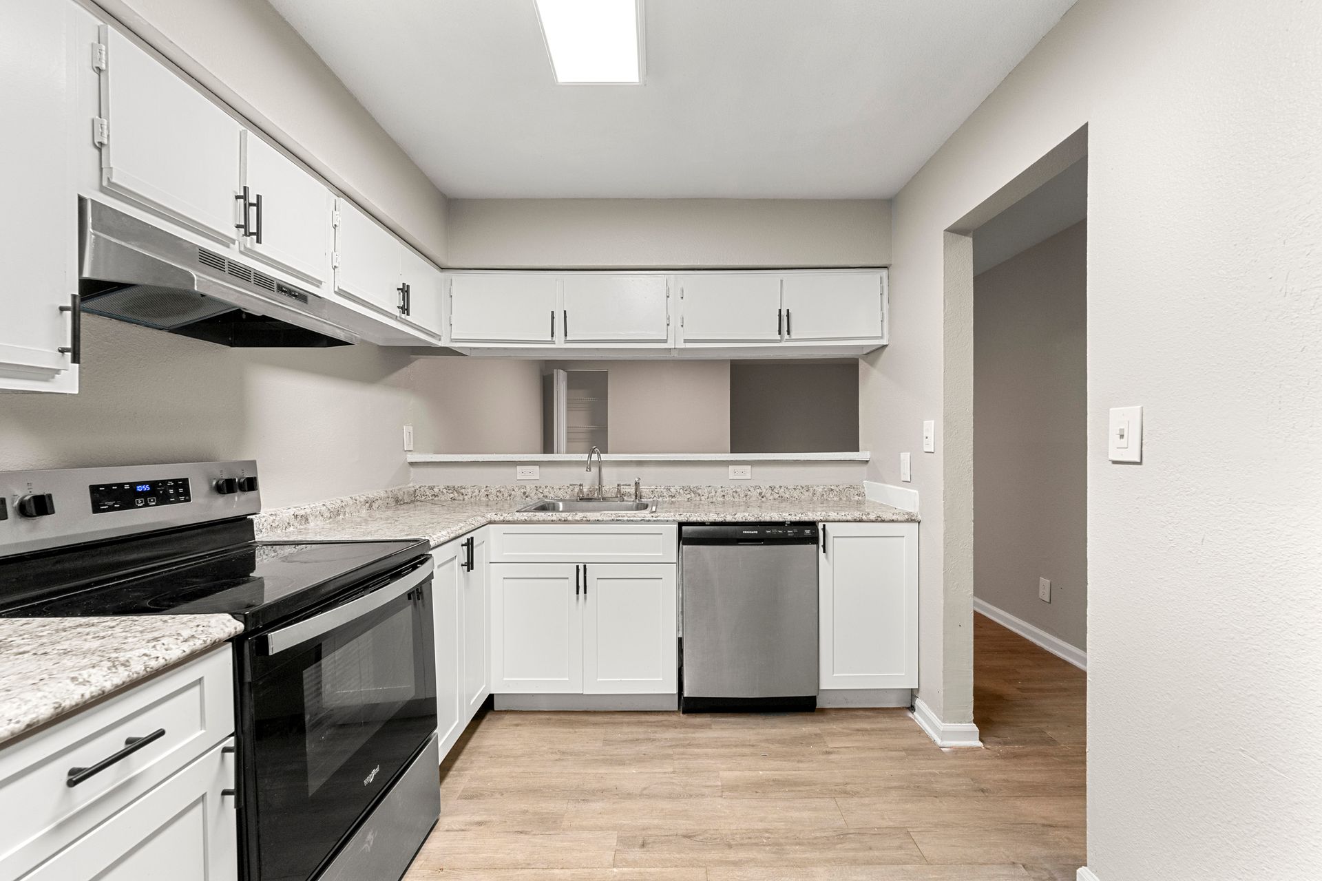 Modern white kitchen with black appliances, light wood floors, and gray walls