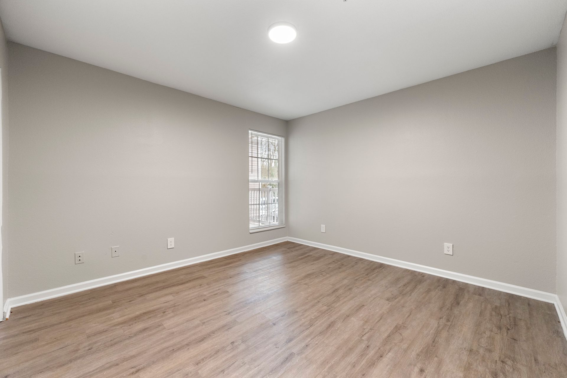 Empty room with gray walls, wood floor, and a small window.