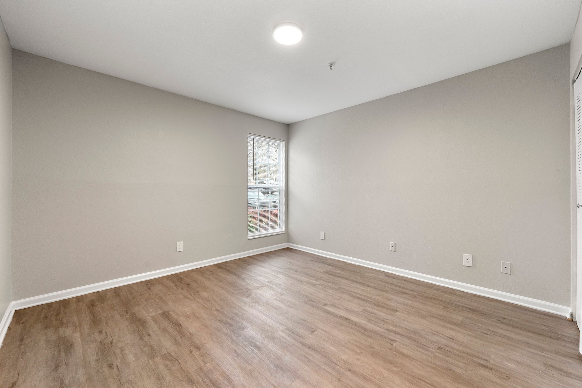 Empty gray bedroom with wood flooring and a narrow window.